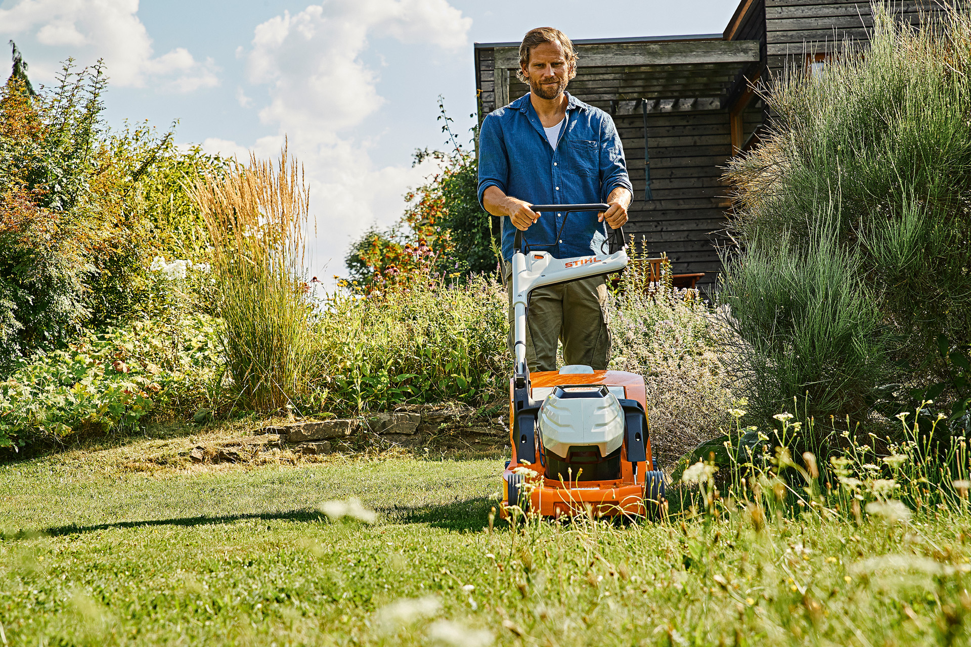 Un hombre en un jardín encargándose de cuidar el césped en verano con su cortacésped de batería STIHL RMA 448