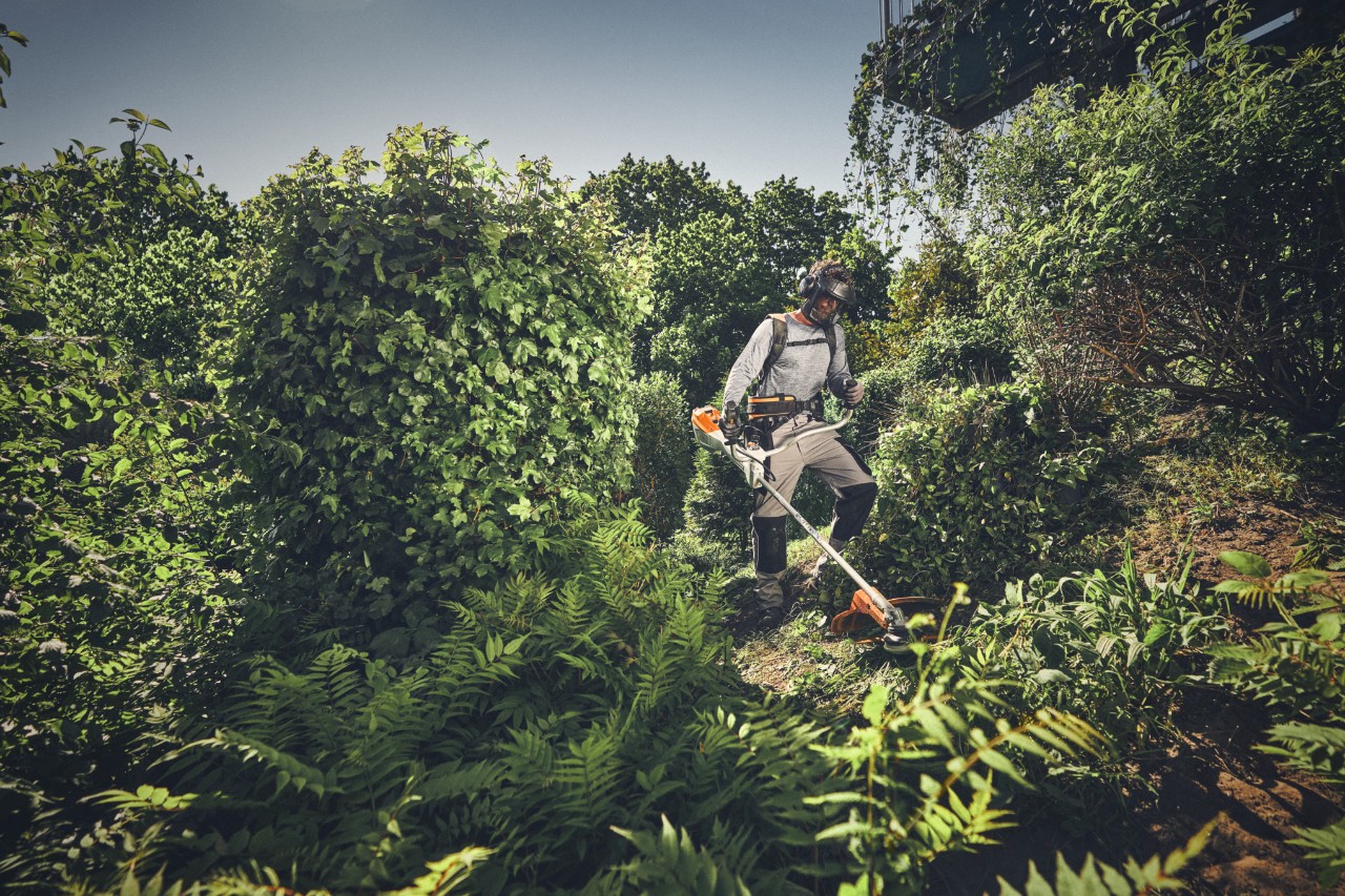 Una persona con equipo de protección corta la maleza que crece salvajemente con una desbrozadora STIHL