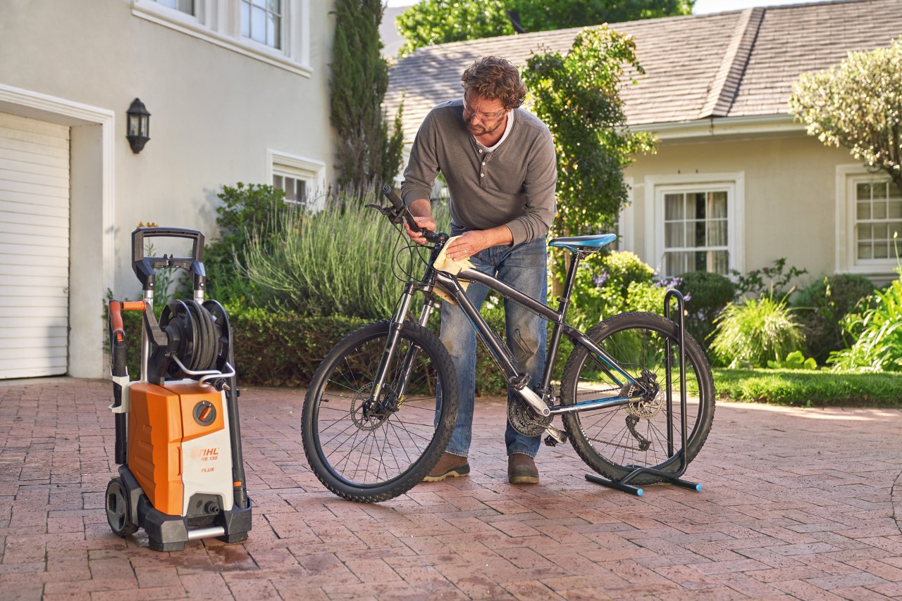 Un hombre seca una bicicleta con un paño junto a una hidrolimpiadora STIHL RE 130 plus