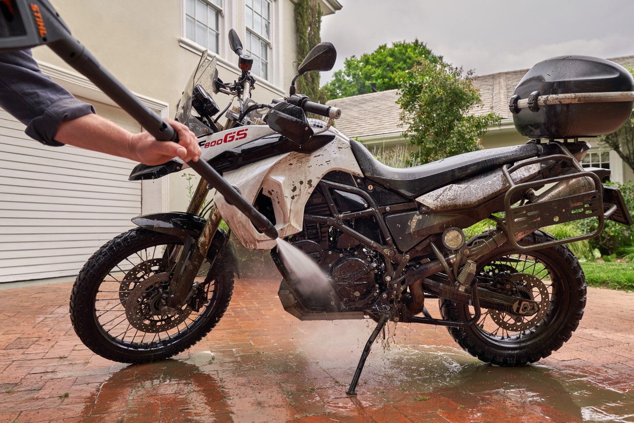 Limpieza de una moto en una entrada frente a una casa blanca con una hidrolimpiadora STIHL RE 130 plus.