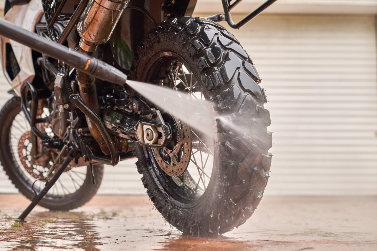 Primer plano de un chorro de agua y de la lanza de una hidrolimpiadora durante la limpieza de una moto.