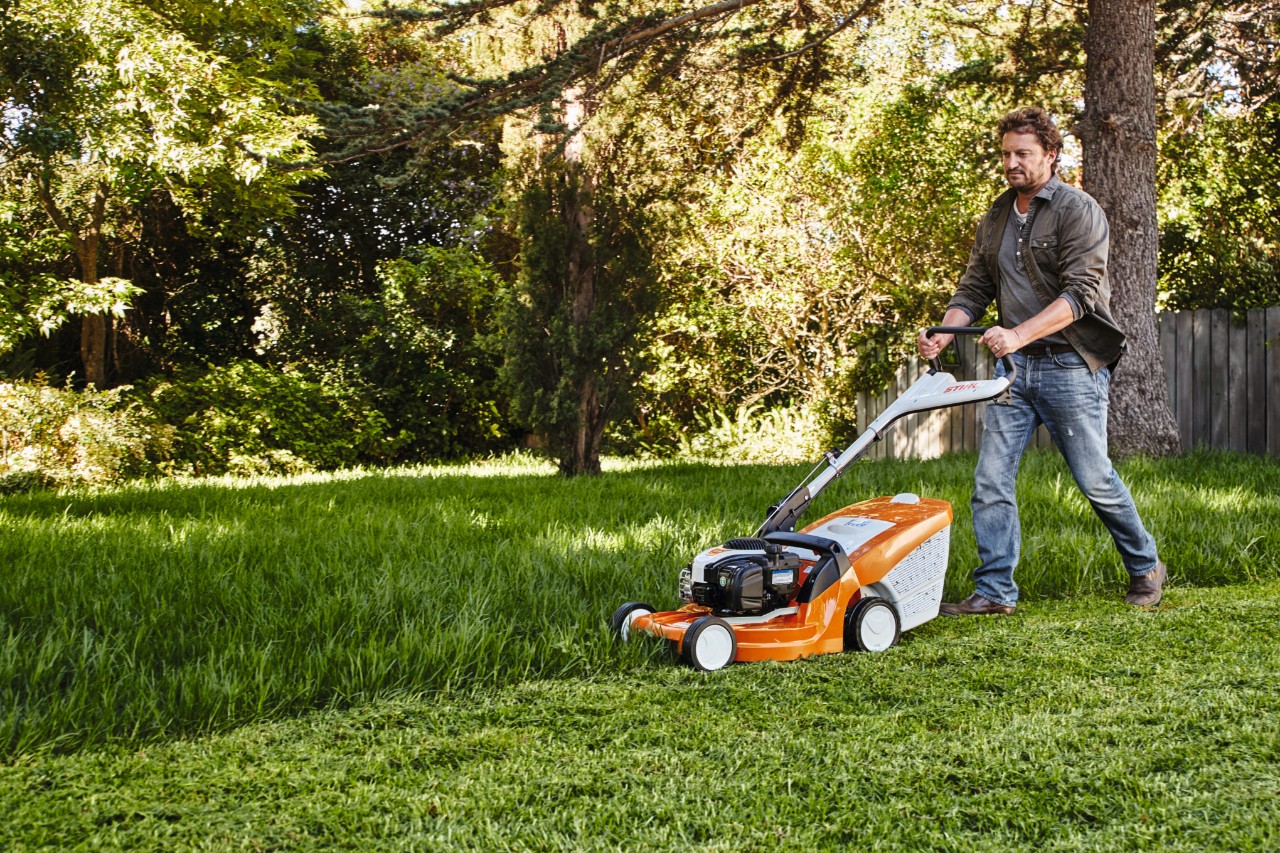 Un hombre corta el césped en un jardín con un cortacésped STIHL. 