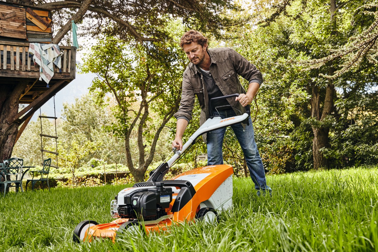 Un hombre corta el césped en un jardín con un cortacésped de gasolina STIHL RM 448 TC