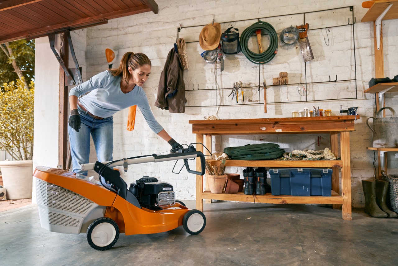 Una mujer prepara el cortacésped de gasolina STIHL RM 448 TC para el invierno en el garaje.