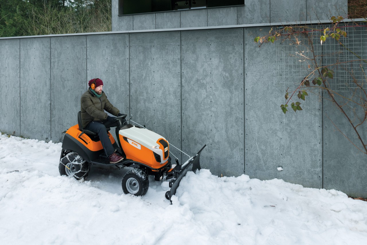 Un hombre retira la nieve de un muro con un tractor de césped con una pala quitanieves 