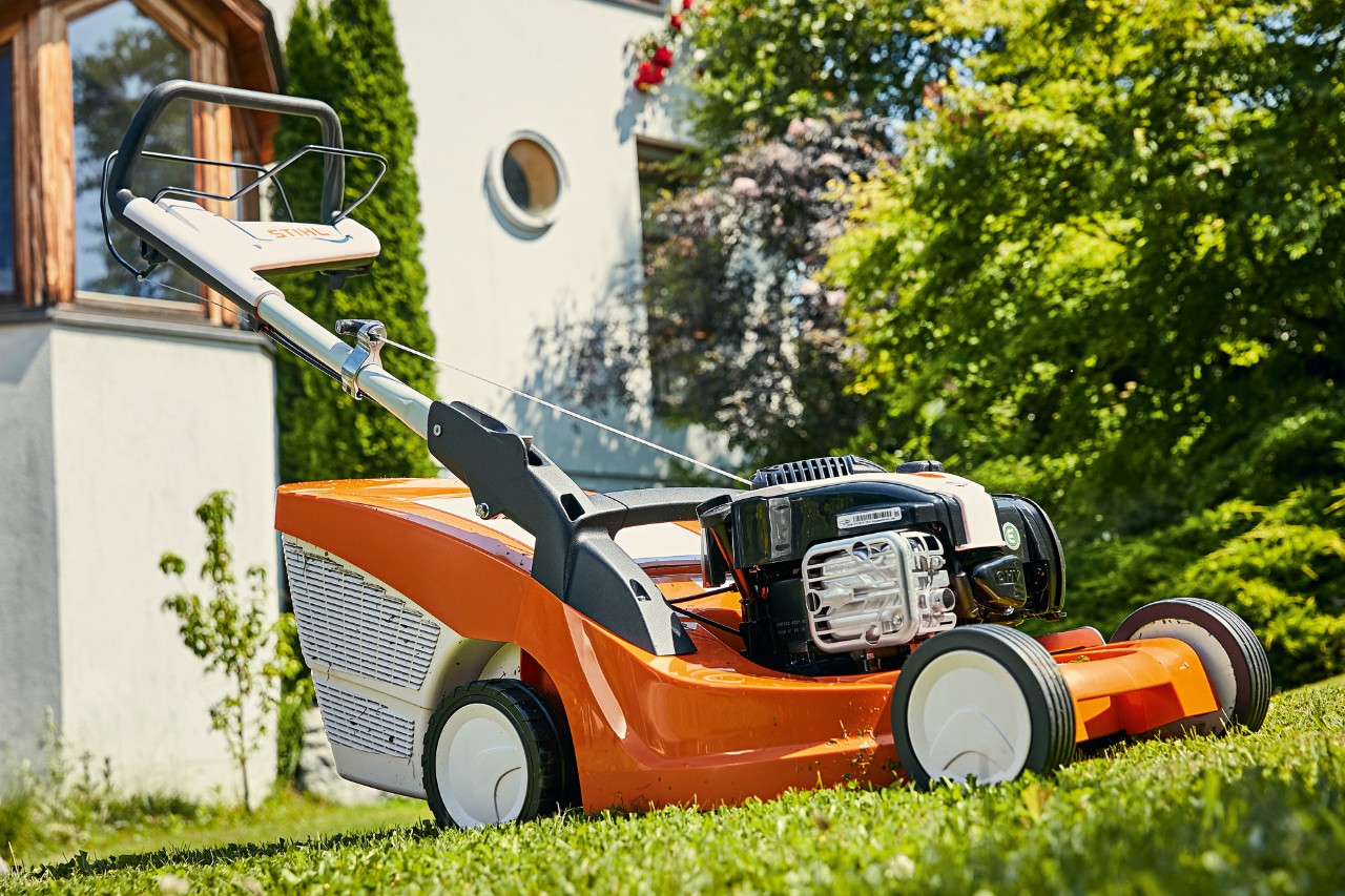 Un cortacésped de gasolina STIHL RM 443 T sobre el césped delante de una casa 