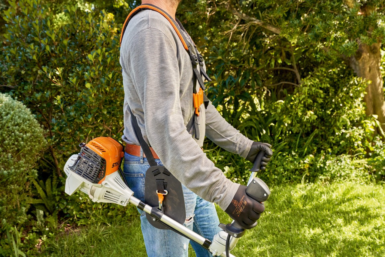 Un hombre levanta la desbrozadora de gasolina STIHL FS 91 del suelo para empezar a cortar 