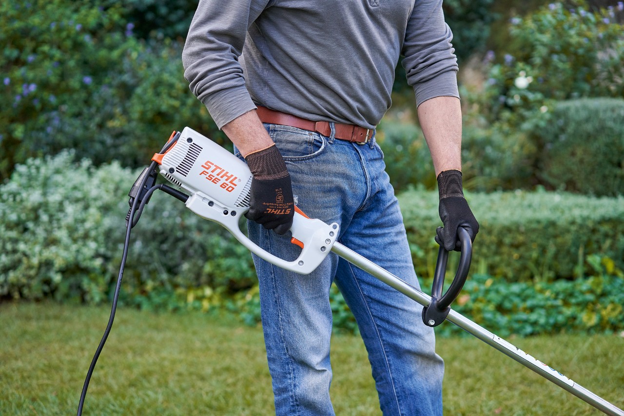 Un hombre con guantes de protección sujeta la desbrozadora eléctrica STIHL FSE 60 con ambas manos