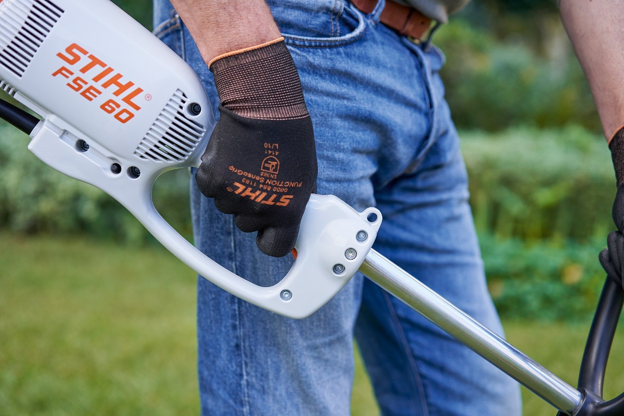 Un hombre pulsa el interruptor en la empuñadura de la desbrozadora eléctrica STIHL FSE 60
