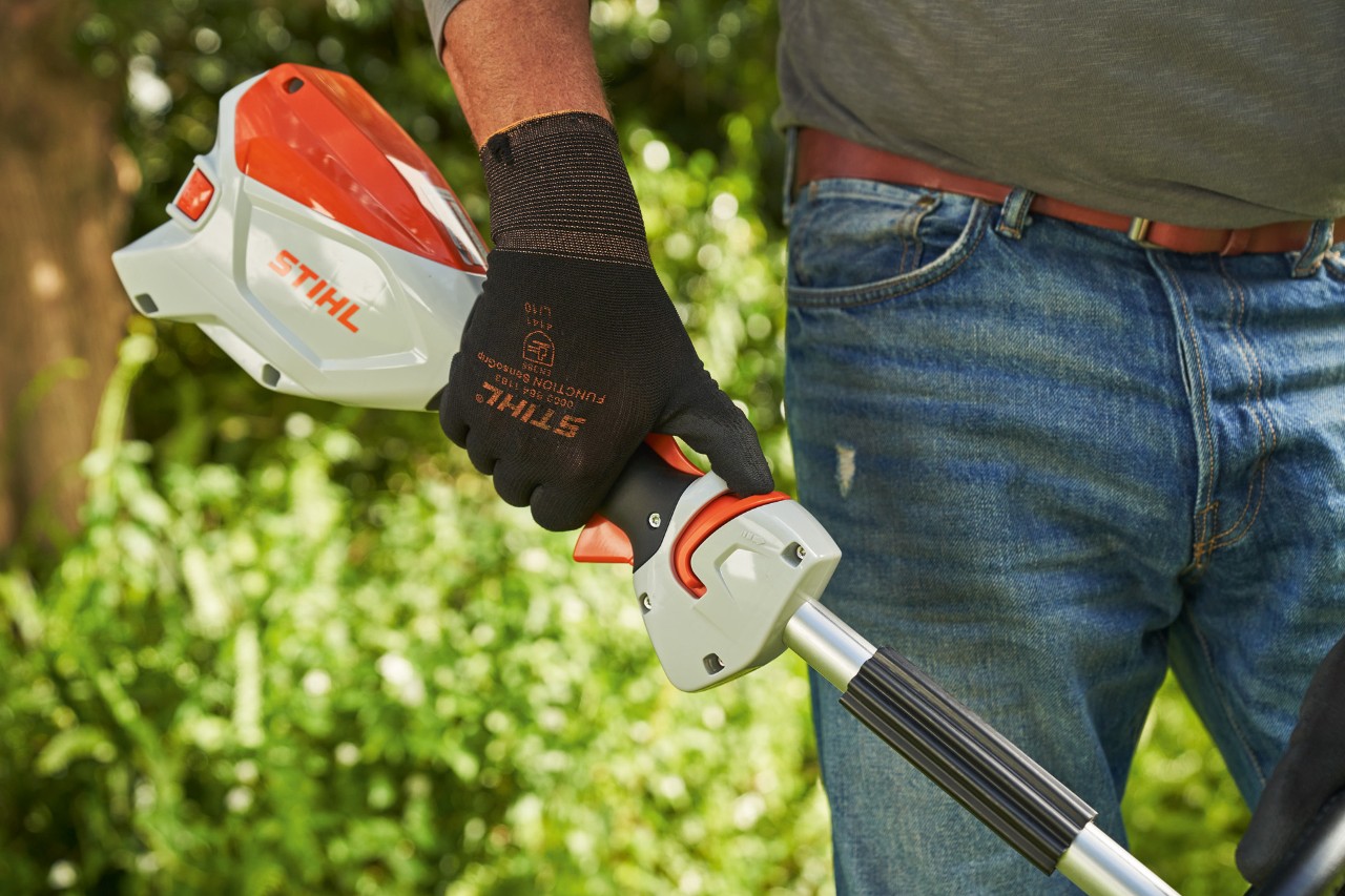 Un hombre con guantes de protección empuja la gatillo de desbloqueo de la desbrozadora de batería STIHL FSA 60 hacia el manillar cerrado