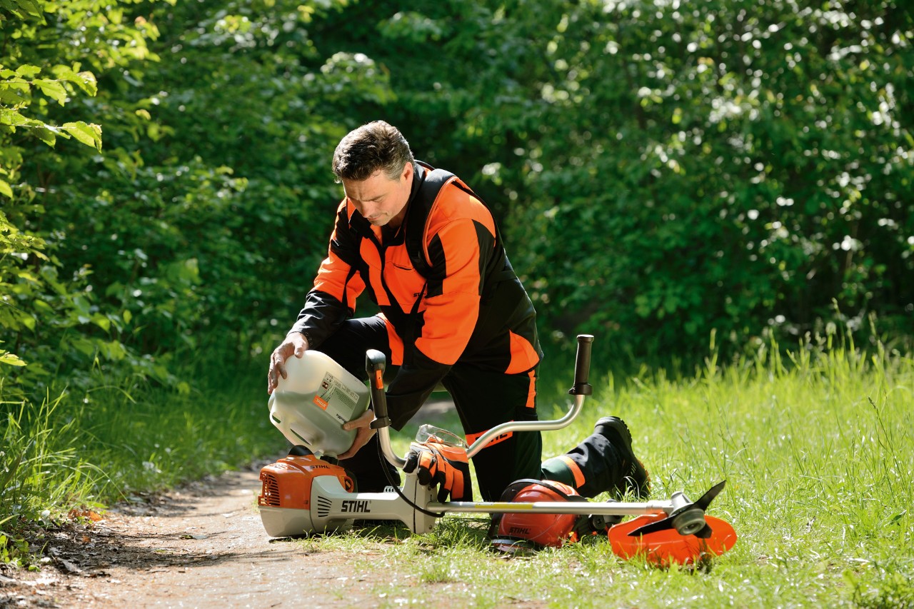 Un hombre con equipamiento de protección STIHL reposta una desbrozadora STIHL con una mezcla de gasolina y aceite