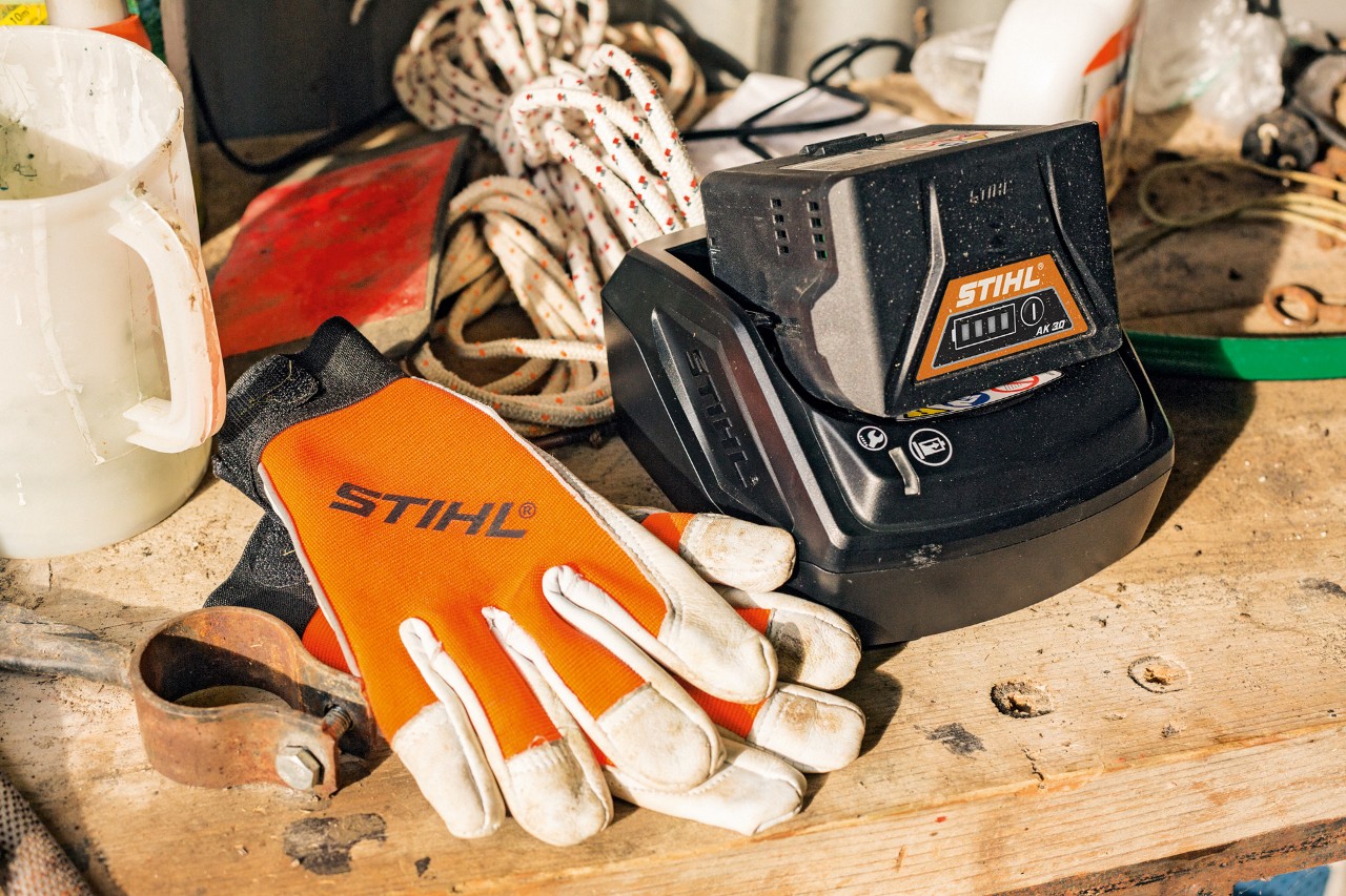 Sobre una superficie de trabajo reposan una batería y unos guantes