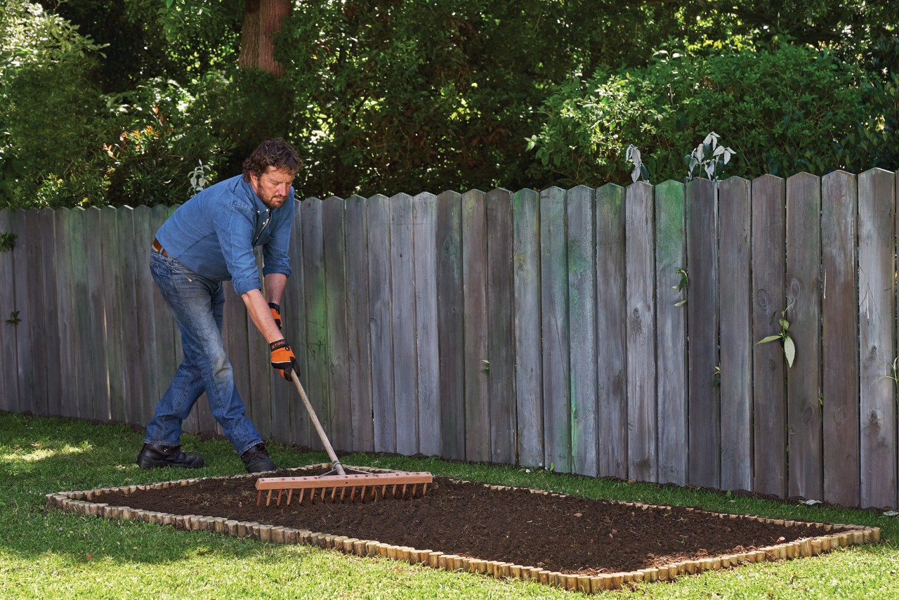 Una persona nivela el suelo con un rastrillo para crear un parterre en un jardín