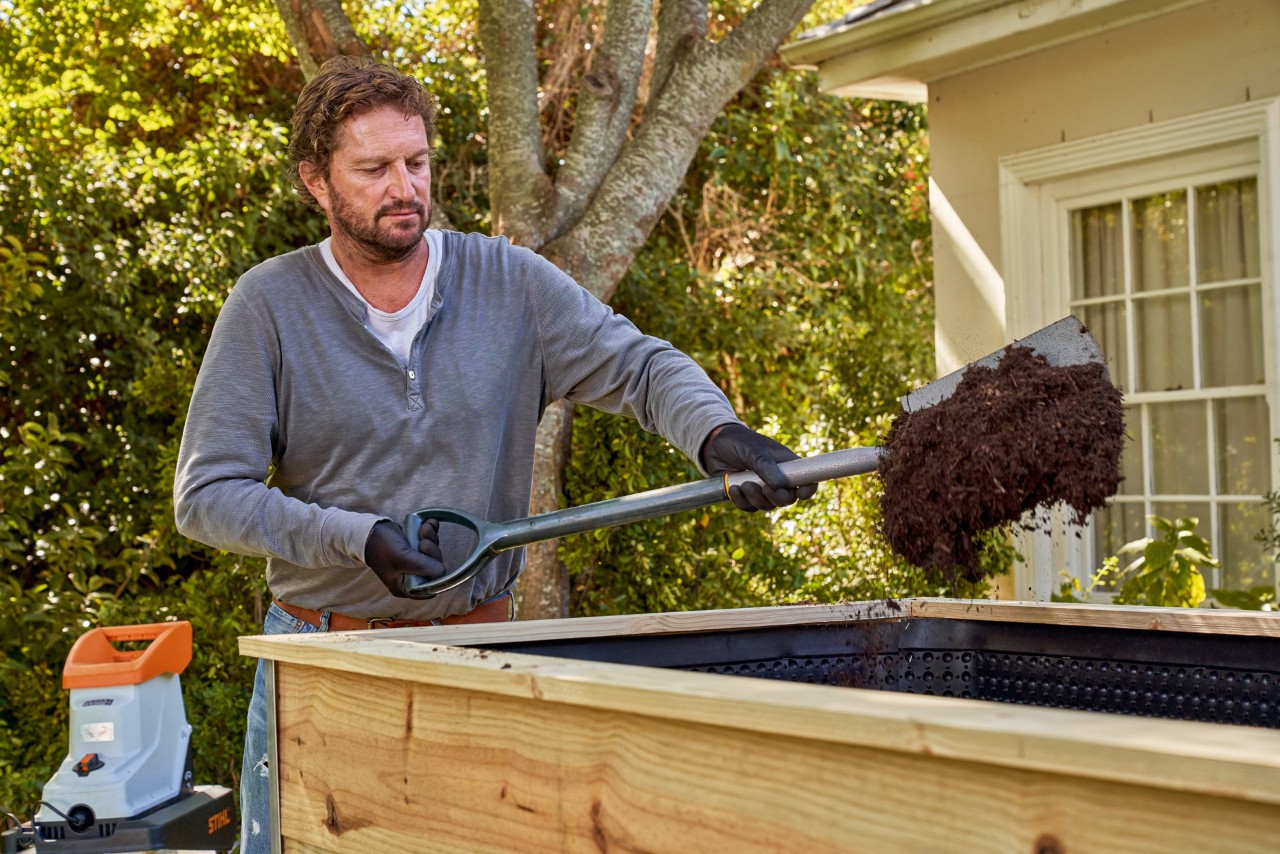 Un hombre utiliza una pala para llenar una mesa de cultivo con compost semiacabado.