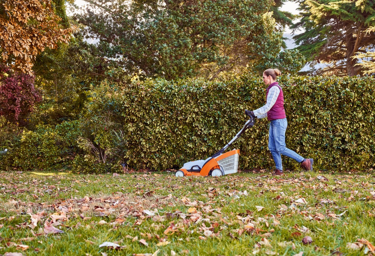 Una mujer se encarga de los cuidados del césped en otoño en un jardín con el cortacésped STIHL RMA 339 C 