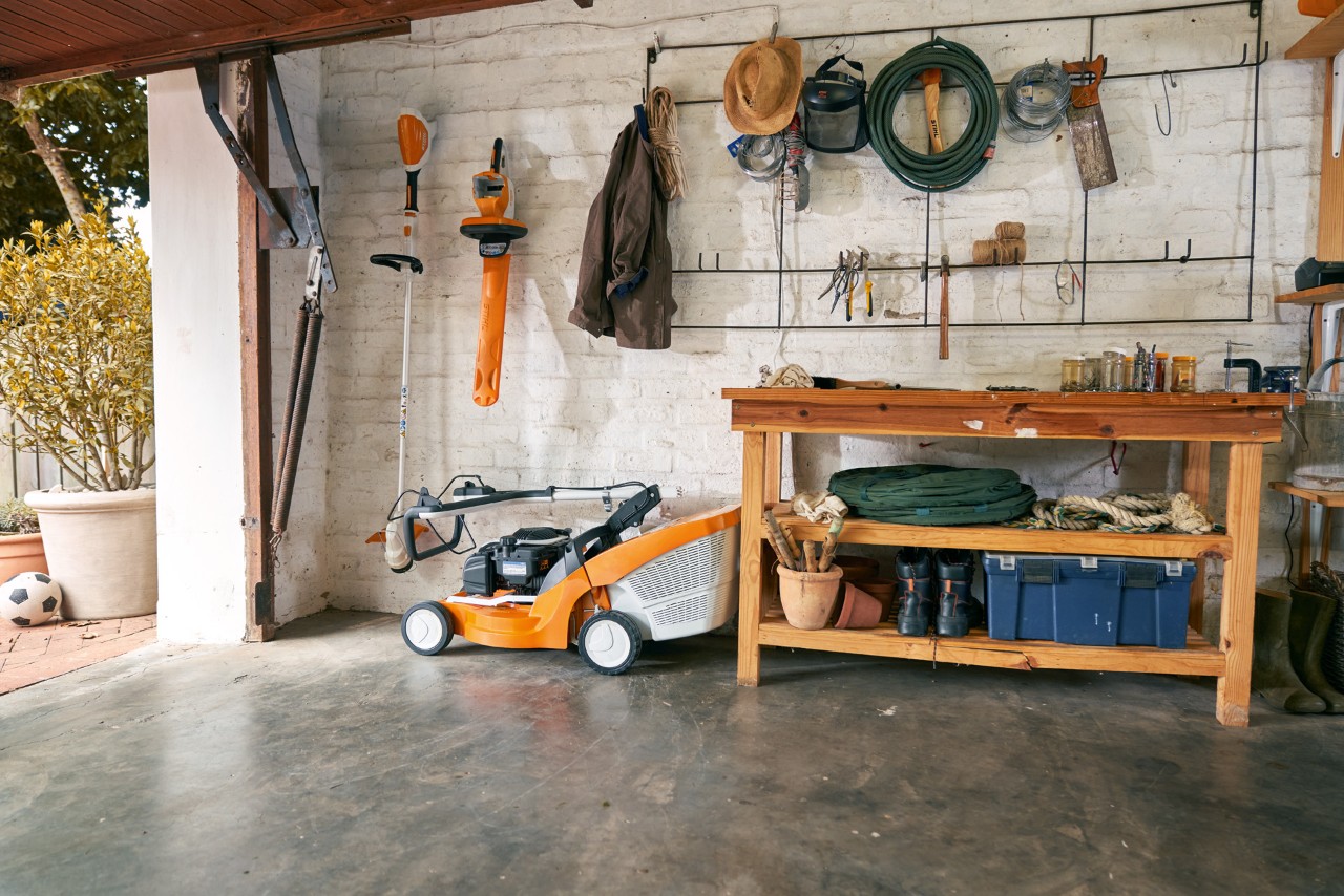 A STIHL RM 448 TC petrol-driven lawnmower and other garden power tools stored neatly in a garage