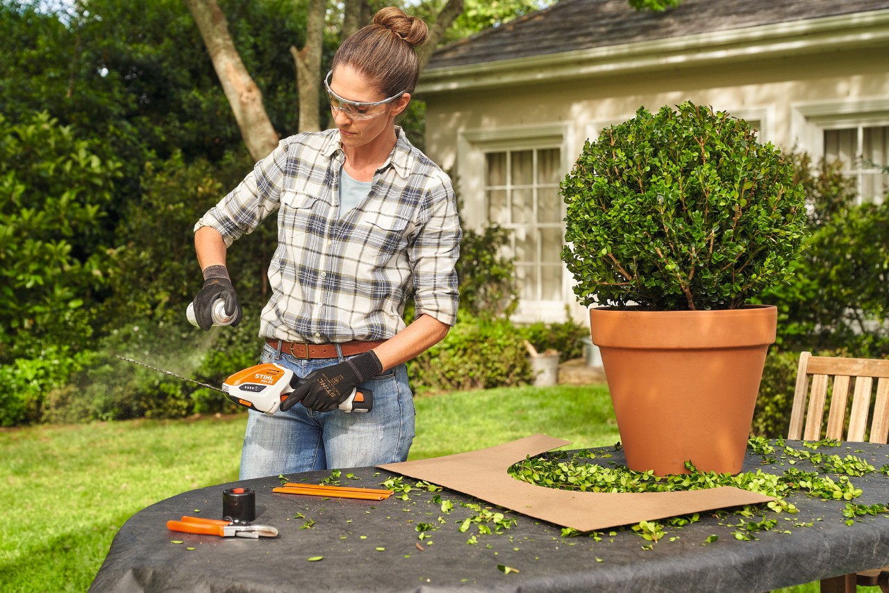 Una mujer pulveriza el cortasetos de batería con el lubricante STIHL Superclean para limpiarlo después de podar