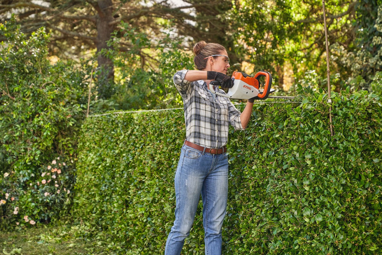 Una mujer corta un seto con el cortasetos de batería STIHL HSA 45