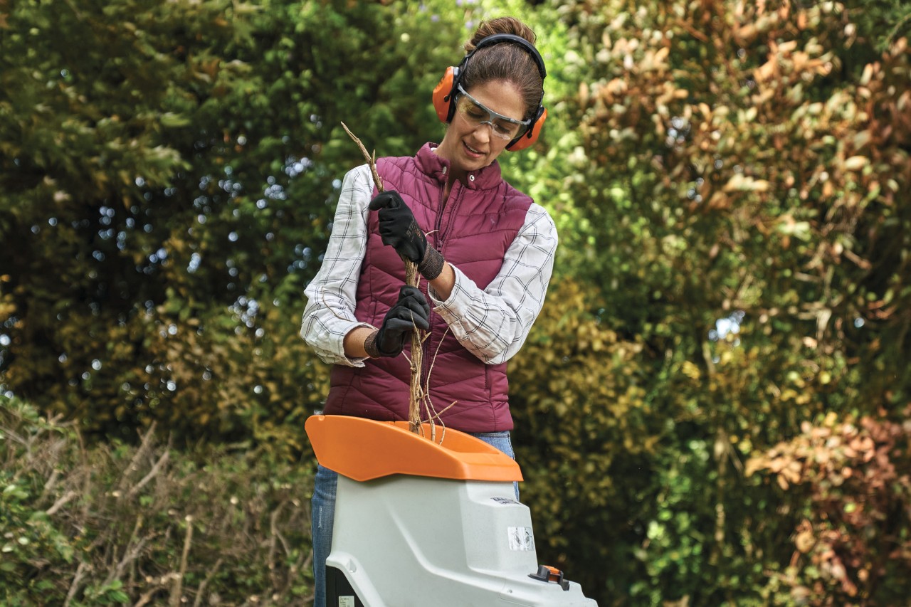 Una mujer con equipamiento de protección individual tritura los recortes de los setos de tuya