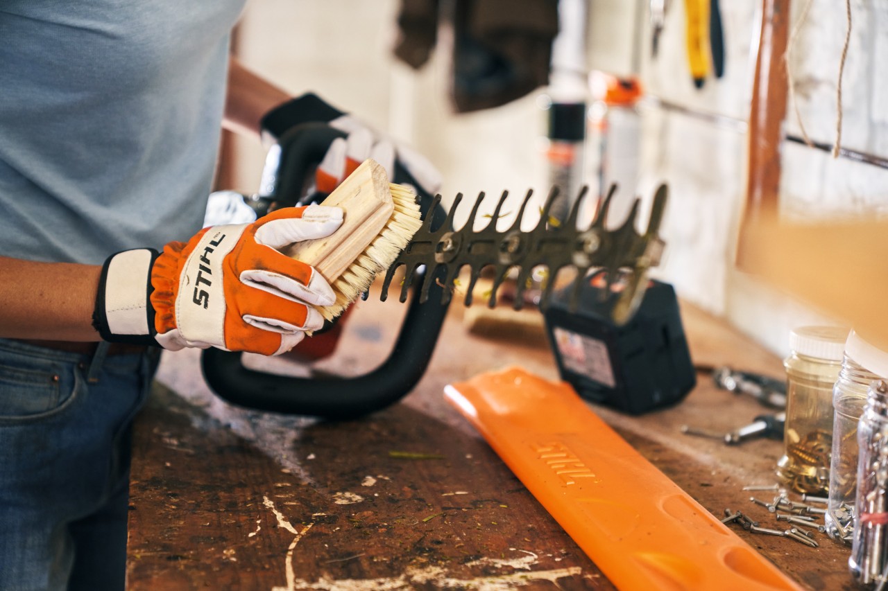 Una persona limpia el cortasetos de batería STIHL HSA 56 con un cepillo en un taller 