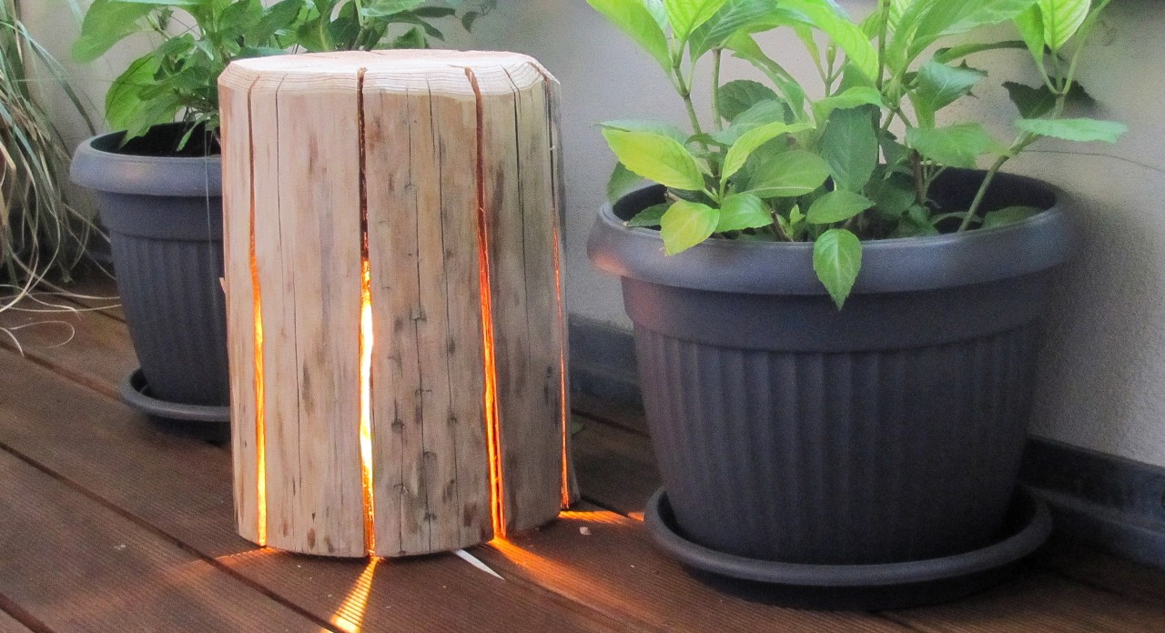 La lámpara de madera de bricolaje se encuentra entre dos macetas; una cadena de luces brilla en el interior