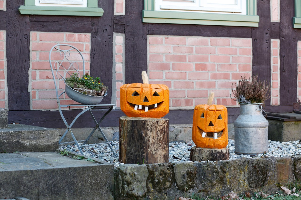 Dos calabazas de madera sobre dos tocones de árbol como decoración delante de una casa