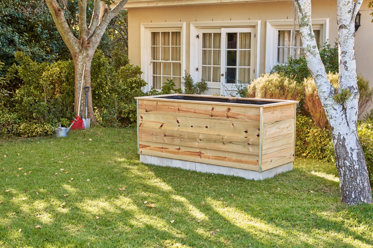 Un huerto elevado de madera de construcción propia en un jardín delante de una casa