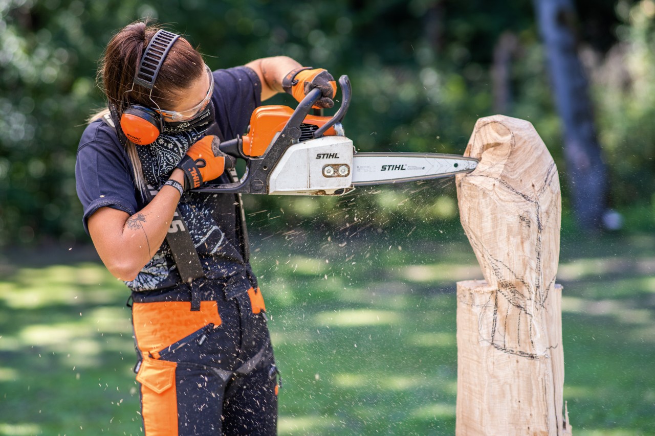 Una mujer con protector de oídos STIHL cortando un búho de madera con una motosierra