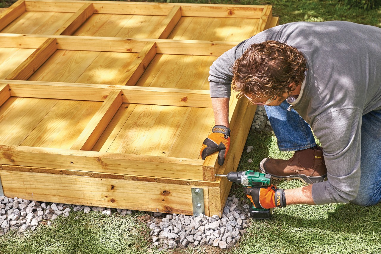 Cómo hacer una caseta de jardín paso a paso: un hombre atornilla una pared de marco y panel para una caseta de jardín.