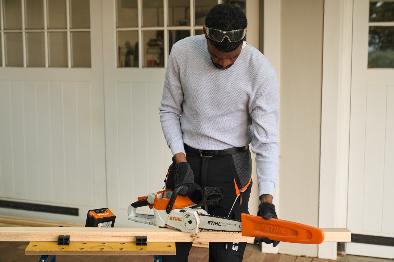 Un hombre delante de un taller retira la protección de una motosierra de batería STIHL MSA 70 
