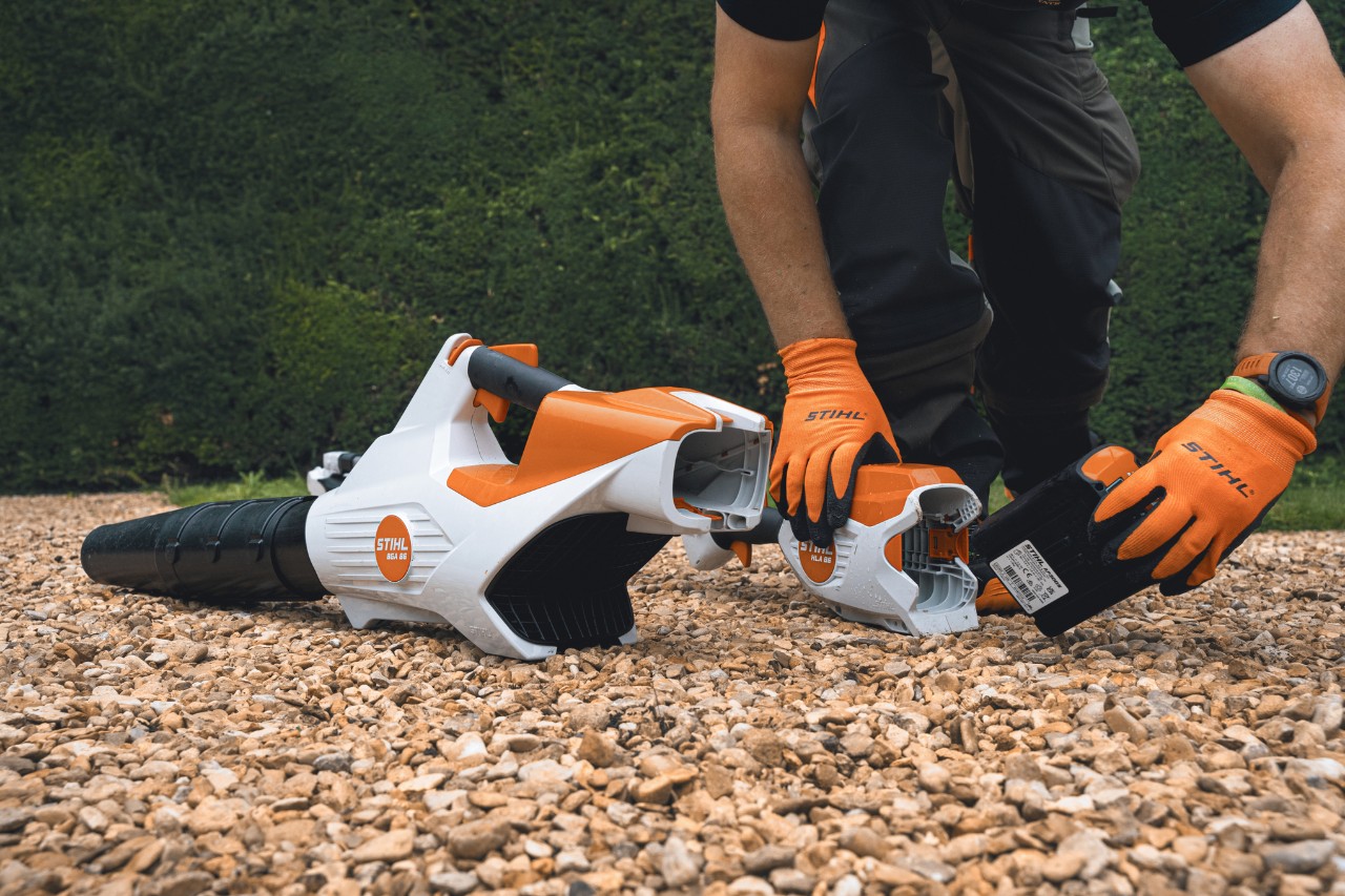 Un profesional cambia la batería de su soplador de batería STIHL delante del seto de Bathurst Estate