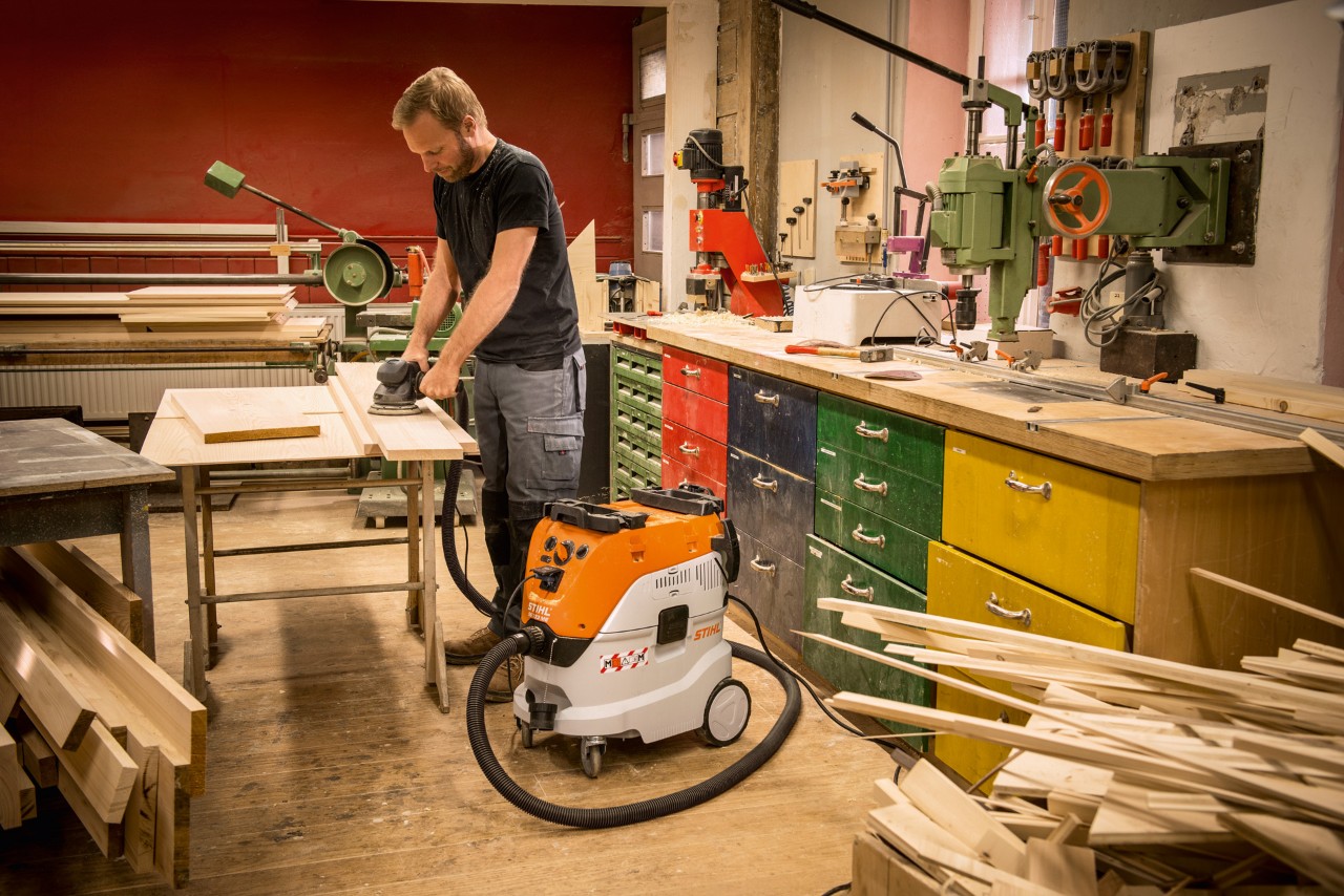 Un hombre utiliza un aspirador de sólidos y líquidos STIHL SE 133 ME para la aspiración de polvo en un taller 