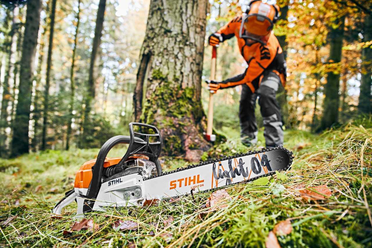 Un hombre con un equipamiento de protección en el bosque; en primer plano, una motosierra de gasolina STIHL MS 261 C-M con espada Light 04