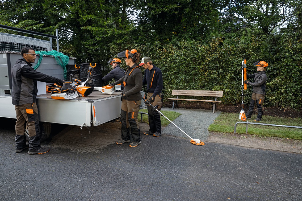 Un grupo de paisajistas y jardineros utilizan máquinas de batería STIHL AP y una batería de mochila de la plataforma de carga del vehículo. 